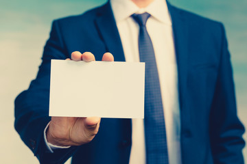 Male hand of a businessman in a blue suit with a tie holds an empty sheet in his hand and shows it to the camera closeup.