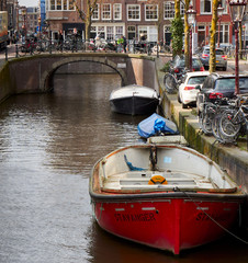 Red boat on the Amsterdam canal with a view of a bridge