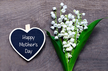 Bouquet of lilies of the valley and decorative heart with Happy Mother's Day text on wooden background.Lily-of-the-valley flowers. Spring festive concept.Selective focus.