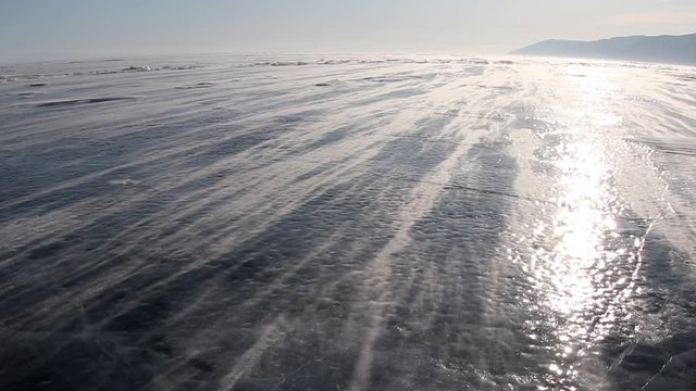Snow blowing on ice from a strong wind on Lake Baikal in winter at sunset, Russia Siberia