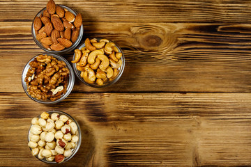 Assortment of nuts on wooden table. Almond, hazelnut, walnut and cashew in glass bowls. Top view, copy space. Healthy eating concept