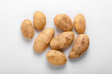 Heap of raw unwashed yellow potatoes over white background, top view