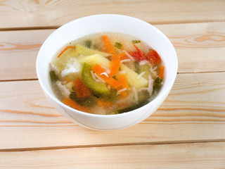 Chicken soup with vermicelli and vegetables. Soup in a white round bowl on a wooden surface. Side...
