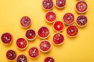 Fresh blood orange halves scattered on a yellow background, top view