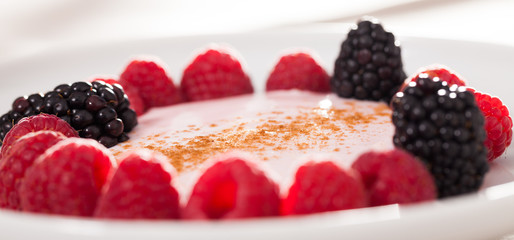 raspberries and blackberries laid out on a white plate in circle with yogurt and cinnamon