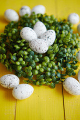 Green decorative Easter quail eggs wreath on yellow wooden table