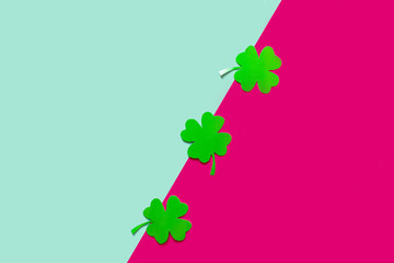Three green clovers on a blue and rose background, flat lay, copy text.