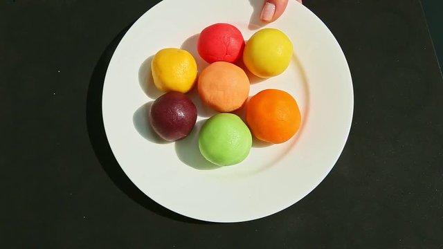 top view on woman hand puts white plate with colored pieces made of marzipan