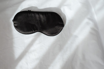 Silk black sleep mask without inscription on white rumpled sheets. Top view, flat lay. Horizontal. Copy spase. Concept of rest, awakening, sleep. For social media, blog. Minimal style