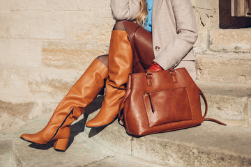 Close up of woman wearing stylish orange boots leather skirt holding purse outdoors. Spring fashion...