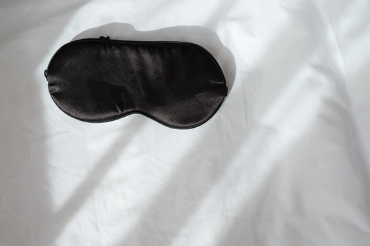 Silk Black Sleep Mask Without Inscription On White Rumpled Sheets. Top View, Flat Lay. Horizontal. Copy Spase. Concept Of Rest, Awakening, Sleep. For Social Media, Blog. Minimal Style