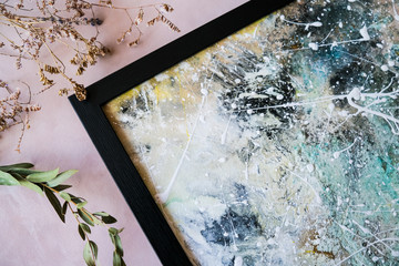 Corner of abstract picture in modern black frame and dried flowers on decorative canvas background.