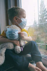 Quarantine, threat of coronavirus. Sad child and his teddy bear both in protective medical masks...