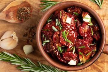 Sun-dried tomatoes with garlic, rosemary and spices in a clay bowl on an olive wood cutting board, top view, flat lay