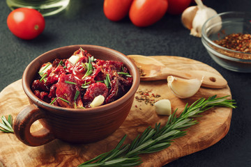 Sun-dried tomatoes with garlic, rosemary and spices in a clay bowl on an olive wood cutting board