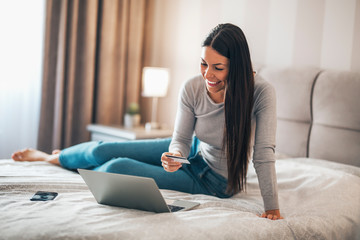 Girl sitting in the bedroom using laptop and credit card for online shopping.