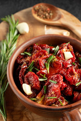 Sun-dried tomatoes with garlic, rosemary and spices in a clay bowl on an olive wood cutting board, vertical image