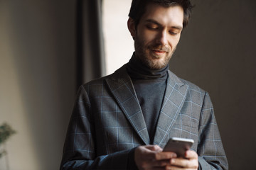 Image of handsome young businessman wearing suit using cellphone in cafe