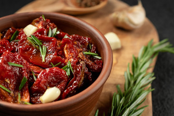 Sun-dried tomatoes with garlic, rosemary and spices in a clay bowl on an olive wood cutting board