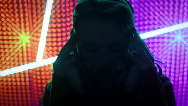 Young girl model in the neon lights of the club. Concept of dubstep or punk style. Wearing a gas mask from dirty air. Protected in a public place from the Chinese coronavirus.
