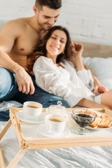 Obraz na płótnie Canvas selective focus of happy young couple near bed tray with delicious breakfast