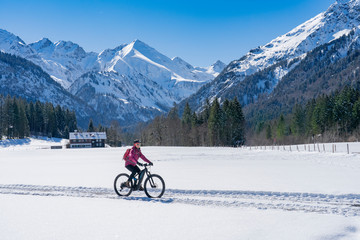 nice senior woman riding her electric mountainbike on a sunny winter day in the Allgau alps near Oberstdorf, Bavaria, Germany