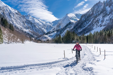 Fototapeta na wymiar nice senior woman riding her electric mountainbike on a sunny winter day in the Allgau alps near Oberstdorf, Bavaria, Germany