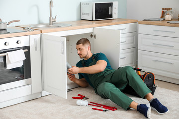 Handsome plumber repairing sink in kitchen