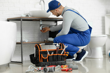 Handsome plumber repairing sink in bathroom - obrazy, fototapety, plakaty