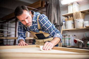 Professional carpenter polishing wood using abrasive paper in carpentry workshop