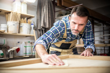 Professional carpenter polishing wood using abrasive paper in carpentry workshop - obrazy, fototapety, plakaty