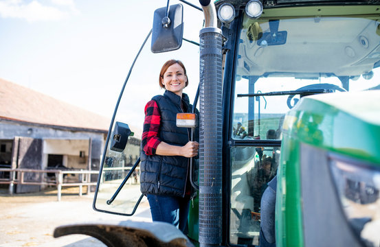 Woman worker standing by tractor on diary farm, agriculture industry.