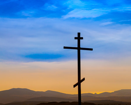 Black religion symbol silhouette Jesus Christ wooden cross on a background with colorful mountain sunset, Easter concept.