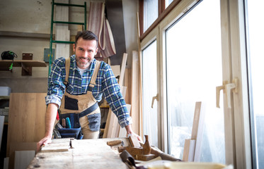 Portrait of mature carpenter posing in his carpentry workshop with tools in background - obrazy, fototapety, plakaty