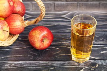 A glass of apple juice and red apples on a dark wooden background