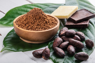 Cacao powder in wooden bowl, whole cacao beans, pieces of dark bitter chocolate and cocoa butter...