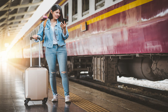 woman travel with luggage using smartphone at train station platform