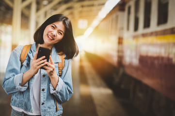 happy woman traveler with smartphone at train station platform