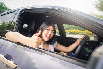 Happy Asian woman driving her new car and showing thumb up