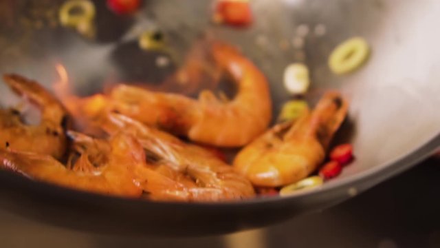 Chef fries prawns with vegetables in a wok with flame, slow motion.