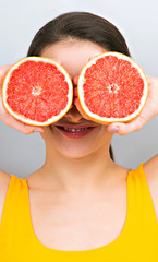 Happy smiling fun woman holding red grapefruit near the face on blue background