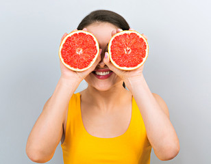 Happy smiling fun woman holding red grapefruit near the face and covering the eyes on blue background. Closeup