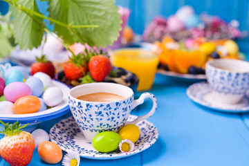 Easter breakfast. Vintage cup with coffee espresso , orange juice, easter colored eggs, granola, honey on a blue wooden background. Copy space