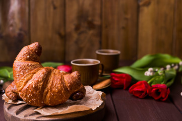 Croissants and red tulips. Easter breakfast with aromatic fresh espresso. Coffee with pastries, flowers on a wooden table. Copy space.
