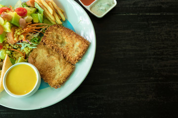 Fish deep-fried steak with salad, french fries, and toast in a white dish on a wooden table. Another delicious menu. Top view and close-up photo.