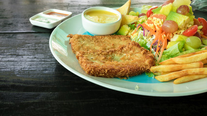 Fish deep-fried steak with salad, french fries, and toast in a white dish on a wooden table. Another delicious menu. Low angle photo and close up.