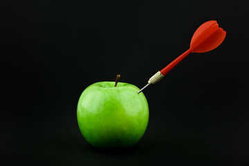 dart sticks out of an apple on a black background. dart hit an apple on a black background
