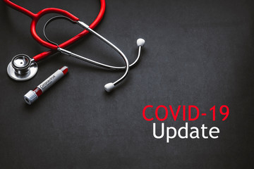 COVID 19 UPDATE text with stethoscope and blood sample vacuum tube on black background. Covid or...