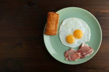 fried eggs and bacon are on the plate on dark wooden background top view with emty space