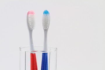 New red and blue plastic toothbrushes in the transparent glass. Bathroom wall. Light blue background. Closeup, copy space.